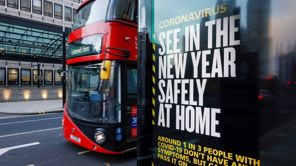A bus drives past a British governments advertisement sign reminding people to stay at home in the New Year, near the Houses of Parliament, in London