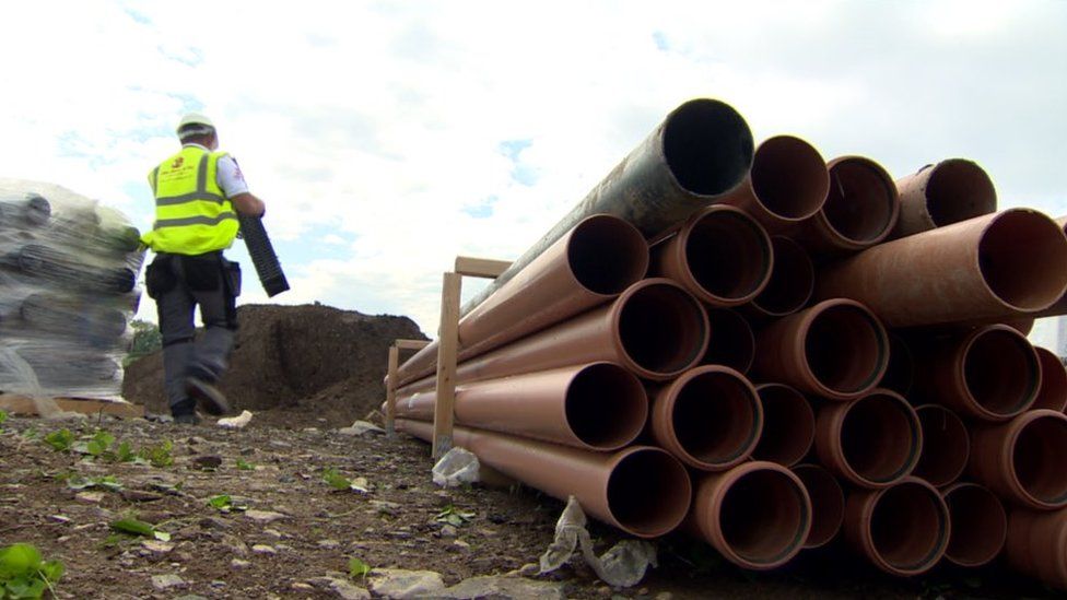 Pipes in the foreground while builder moves supplies
