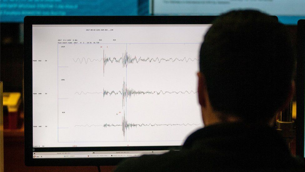 A screen with seismic waves on it, viewed over a man's shoulder