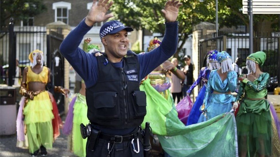 A police officer dances with a group of performers during the Notting Hill Carnival