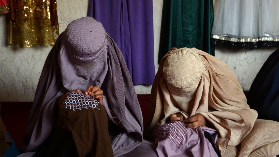 Burqa-clad women stich garments at the workshop of a women run company in Kandahar