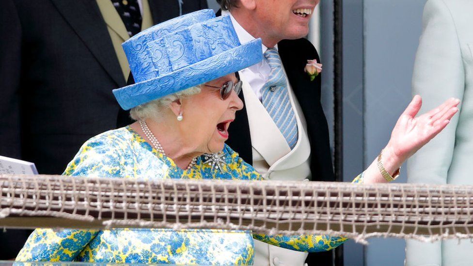 The Queen gesturing with her hand as watches a Derby race intently