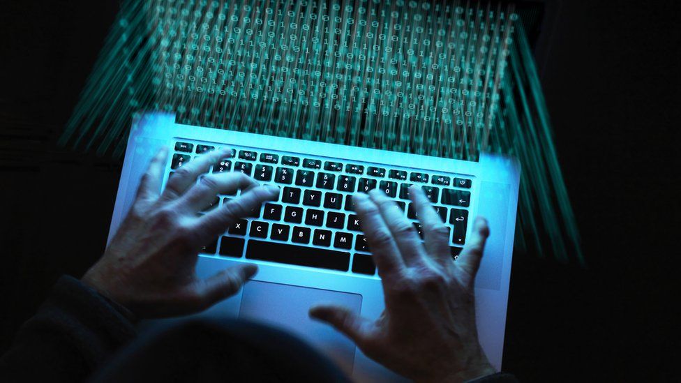 An image of two hands typing on a keyboard pictured from above with a black background, with an effect to make it appear as if the text of the screen is coming out from the screen in green colours