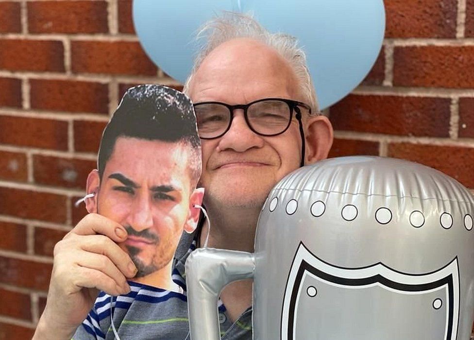 Man holding Gundogan face mask and inflatable cup balloon