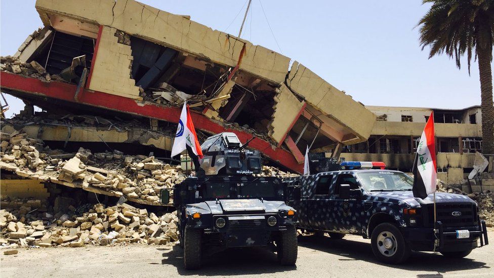 Police vehicles in front of a collapsed building in Mosul