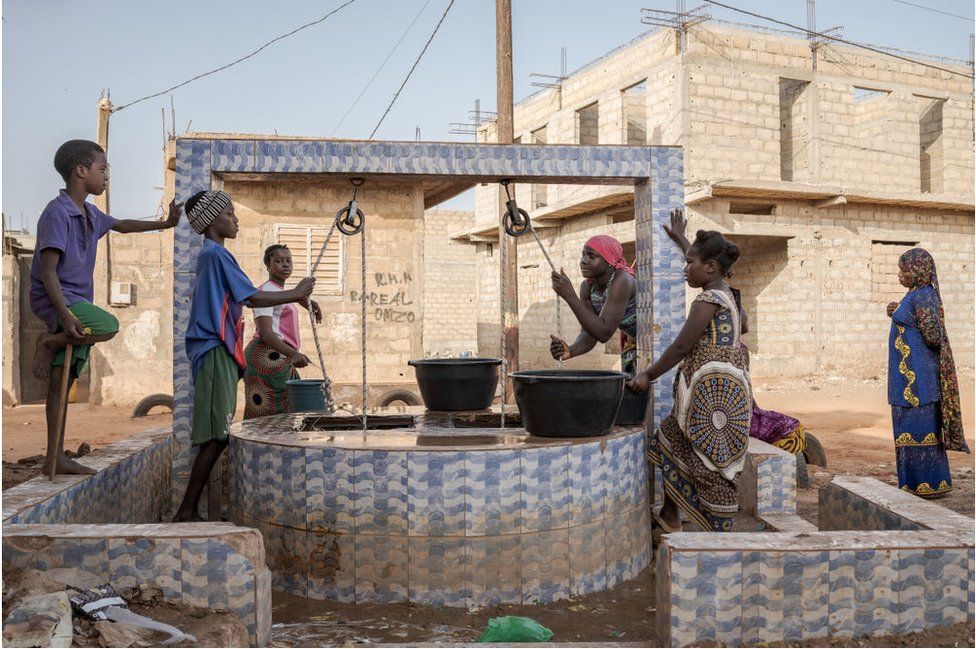 People outdoors getting water from a well.