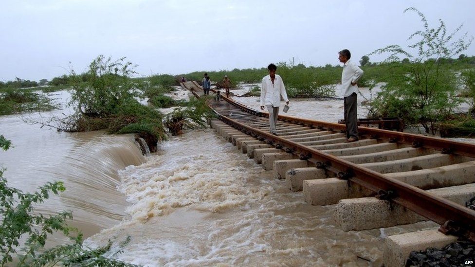 Indian villagers walk along a damaged portion of railway tracks through floodwaters between near Kharaghoda some 120kms. from Ahmedabad on July 29, 2015