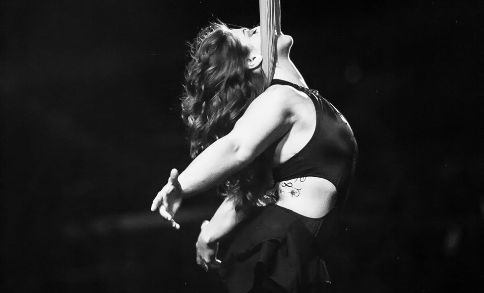 Aerialist Jennifer Bricker hangs by her neck from a silk cloth during her show