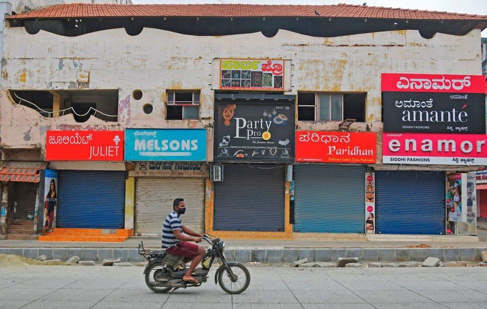 A man rides a two-wheeler in front of closed shops in a commercial area during a week-long lockdown to contain the surge of COVID-19 coronavirus cases, in Bangalore on July 15, 2020.