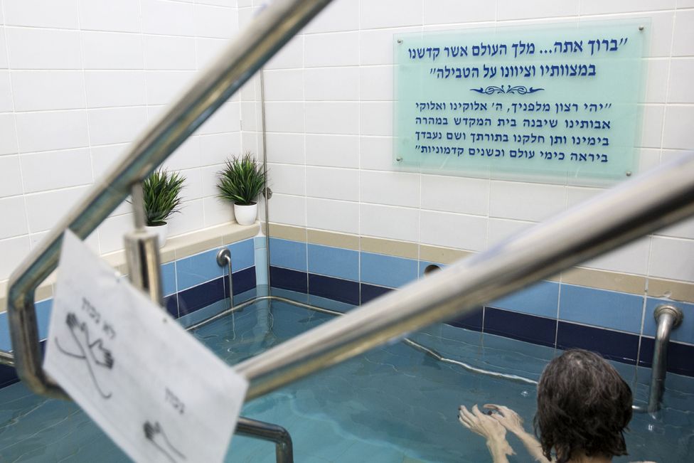 A Jewish woman enters the water of a mikva in Jerusalem on April 17,2019. It is a religious requirement for all married Orthodox women to go to the mikvah, or ritual bath, at night, seven days after their period has finished. It is a way to spiritually purify themselves and has great emotional significance for many women. (Photo by Heidi Levine for The BBC).