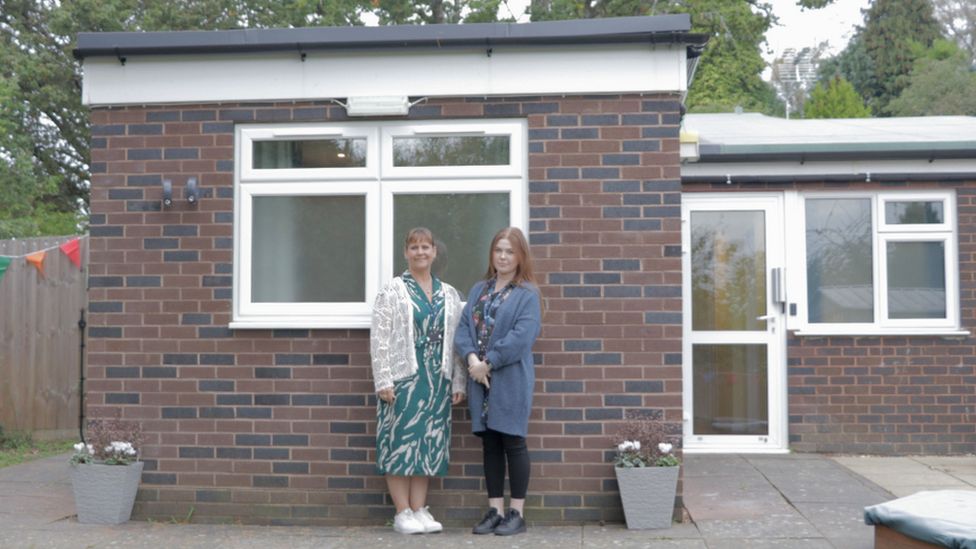 two women stand outside a bungalow