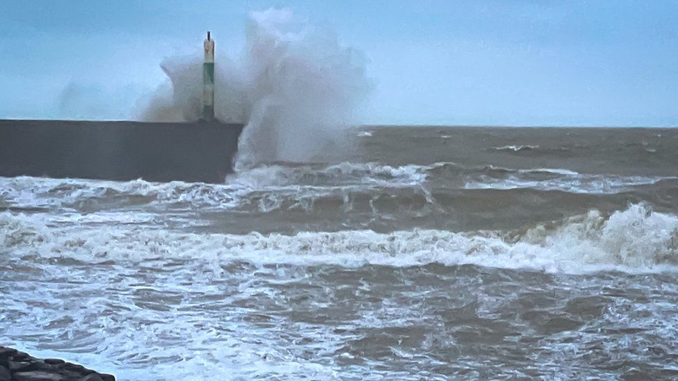 Waves crashing into a pier and light in the Aberystwyth harbour sending spray skyward