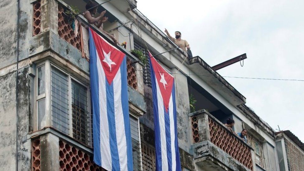 A man hangs a Cuban flag from a rooftop to cover the windows of the house of Yunior Garcia, actor, playwright and leader of the Facebook group called Archipelago, in Havana, Cuba, November 14, 2021