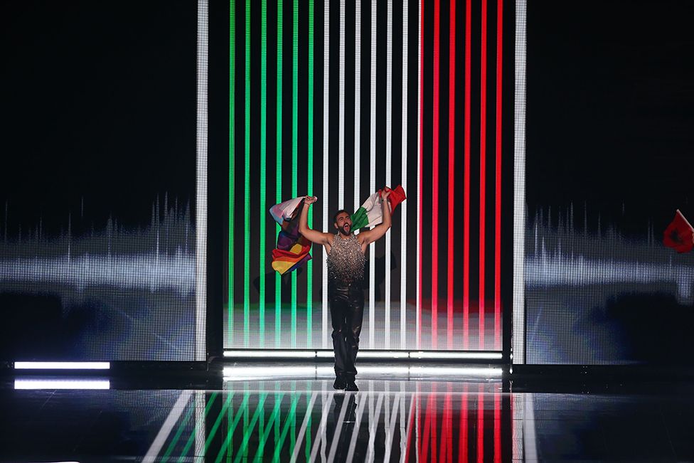 Marco Mengoni of Italy poses on stage with an Italian and Pride flag at the start of the Grand Final