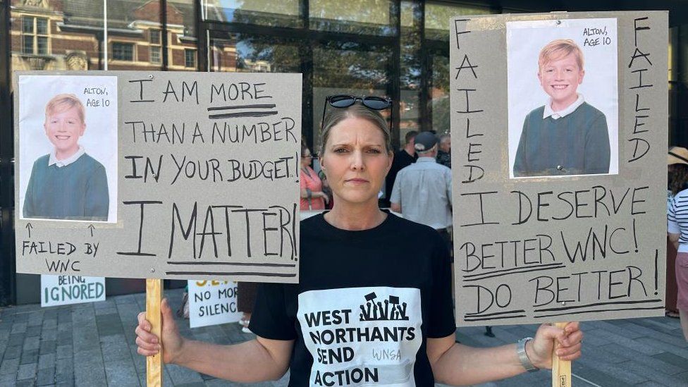 Steph Rocke holds placards showing pictures of her son with slogans saying he has been failed by the council