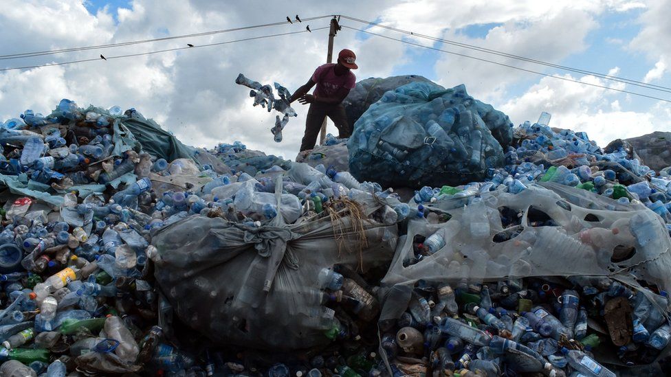 A man stands on top of a pile of plastic rubbish