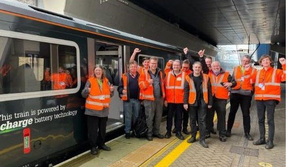 Great Western Railway employees in orange hi-vis jackets standing next to a battery-powered train