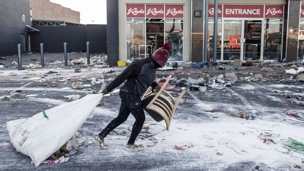 A suspected looter pulls a few items along the ground outside a vandalised mall in Vosloorus, on the outskirts of Johannesburg,