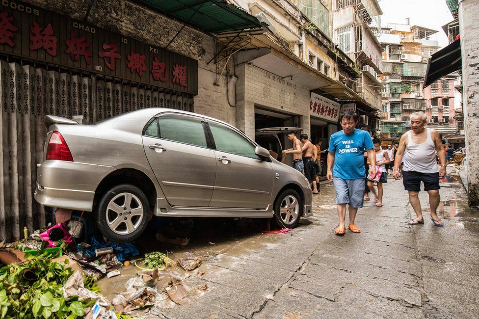 Pedestrians pass by a car on a street after the passage of Typhoon Hato in Macau, China, 23 August 2017.
