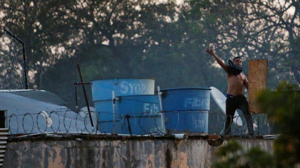 Заключенный бросает камень во время беспорядков в тюрьме Такумбу после того, как заключенные взяли в заложники дюжину чиновников и устроили пожар, в Асунсьоне, Парагвай, 10 октября 2023 года.