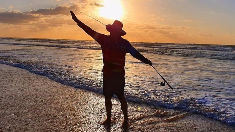 Man fishing on a beach at sunset