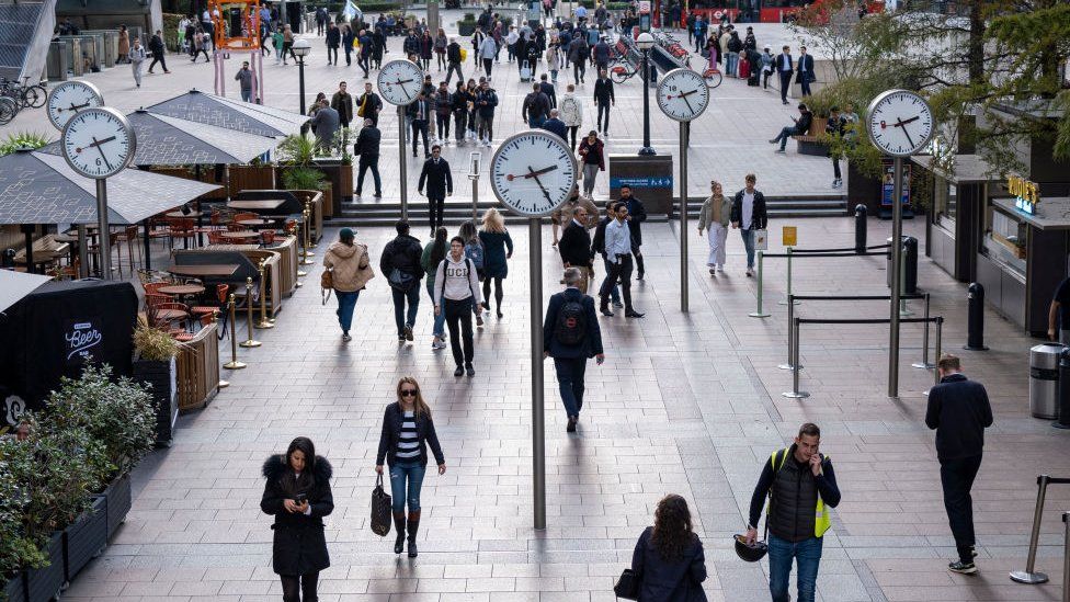 Commuters walking past world clocks in a square in Canary Wharf.