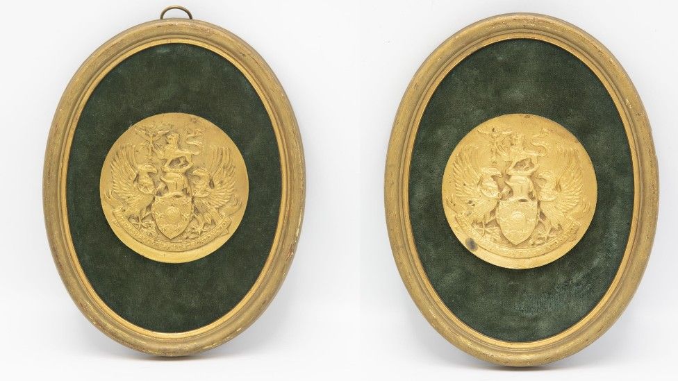 Two identical round gold medals in gold oval frames.