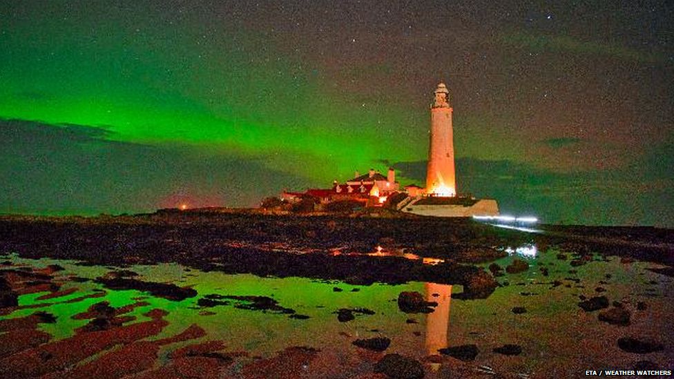 Lighthouse in Whitley Bay with green aurora in the sky behind and reflected in the water in the foreground