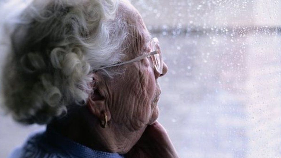An elderly woman looking out of a rain-soaked window