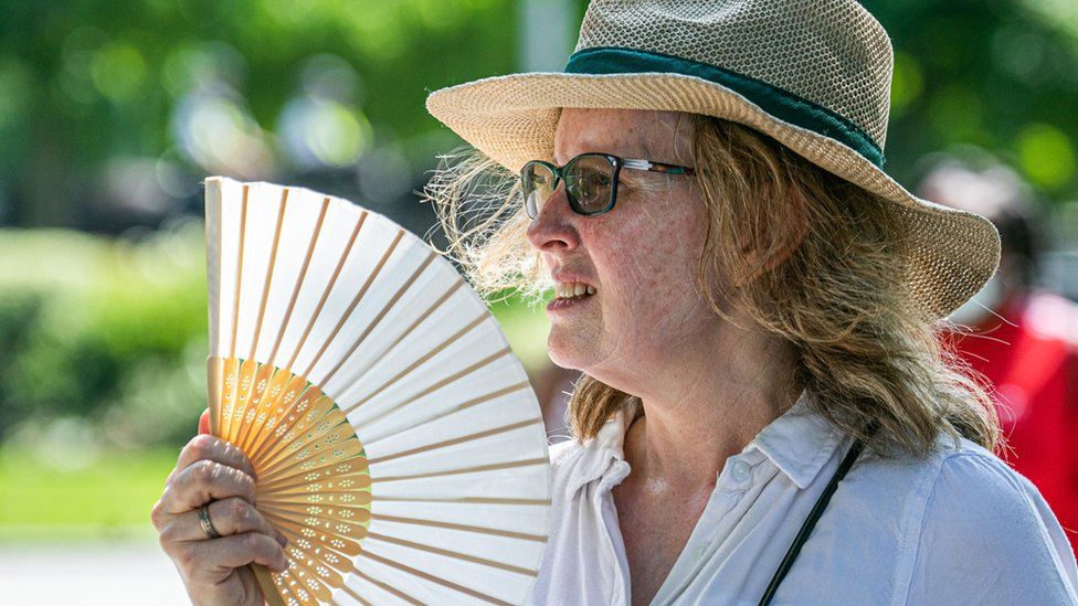 A woman cooling down with a fan on a hot and humid day in London