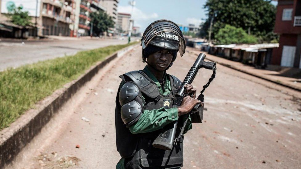 A Police officer is seen in front of protesters, as they continue to throw stones and block roads during mass protests after preliminary results were released in Conakry on October 23, 2020.