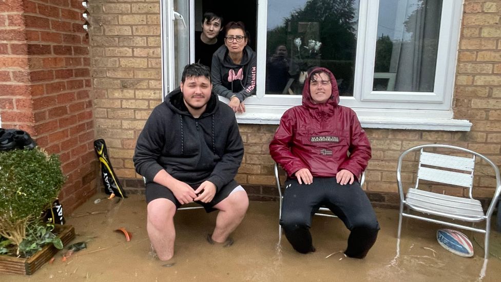 People smiling outside a house flooded in Mold, Flintshire