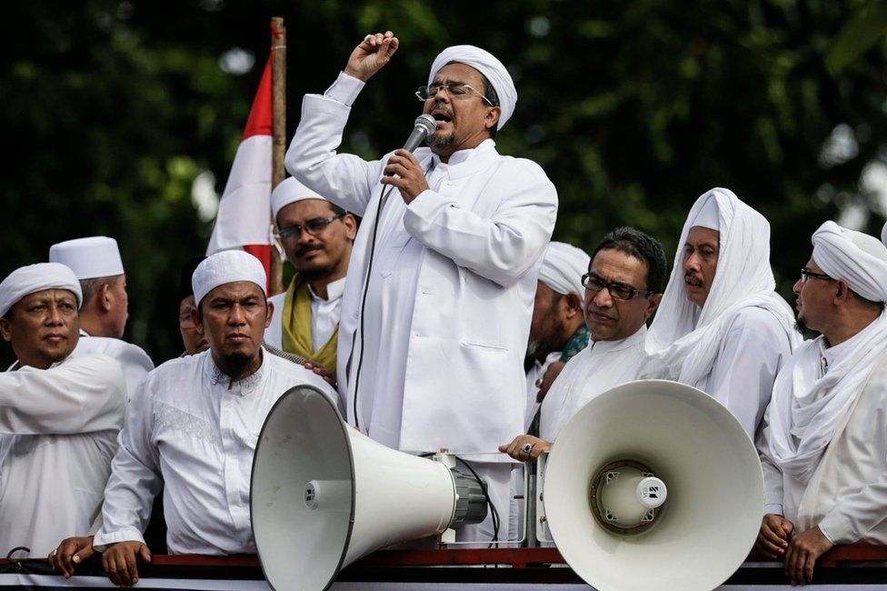 The Leader of the Islamic Defenders Front (FPI), Habib Rizieq (centre, surrounded by supporters in white robes) speaks to supporters by megaphone, outside the police headquarters in Jakarta, Indonesia, 23 January 2017.