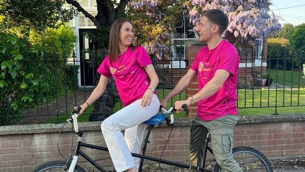 Ms Lowe and Mr Walklin wearing pink tshirts and sitting on a tandem bike