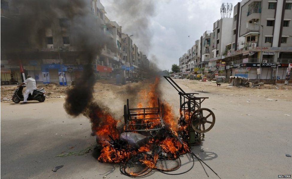 A man on a scooter stands next to burning vehicles after the clashes between the police and protesters in Ahmedabad, India, August 26, 2015.