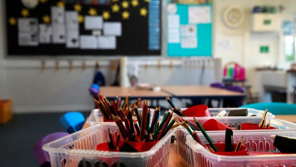 An empty classroom, with stationary containers filled with pencils in the foreground of the picture, and a blurred background