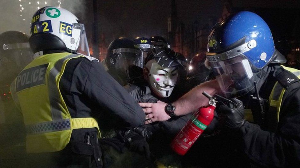 Protesters wearing Guy Fawkes-style being held by police