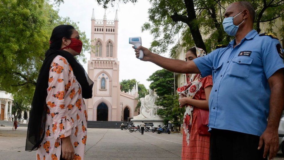 A private security guard checks the temperature of a devotee before mass, in Hyderabad