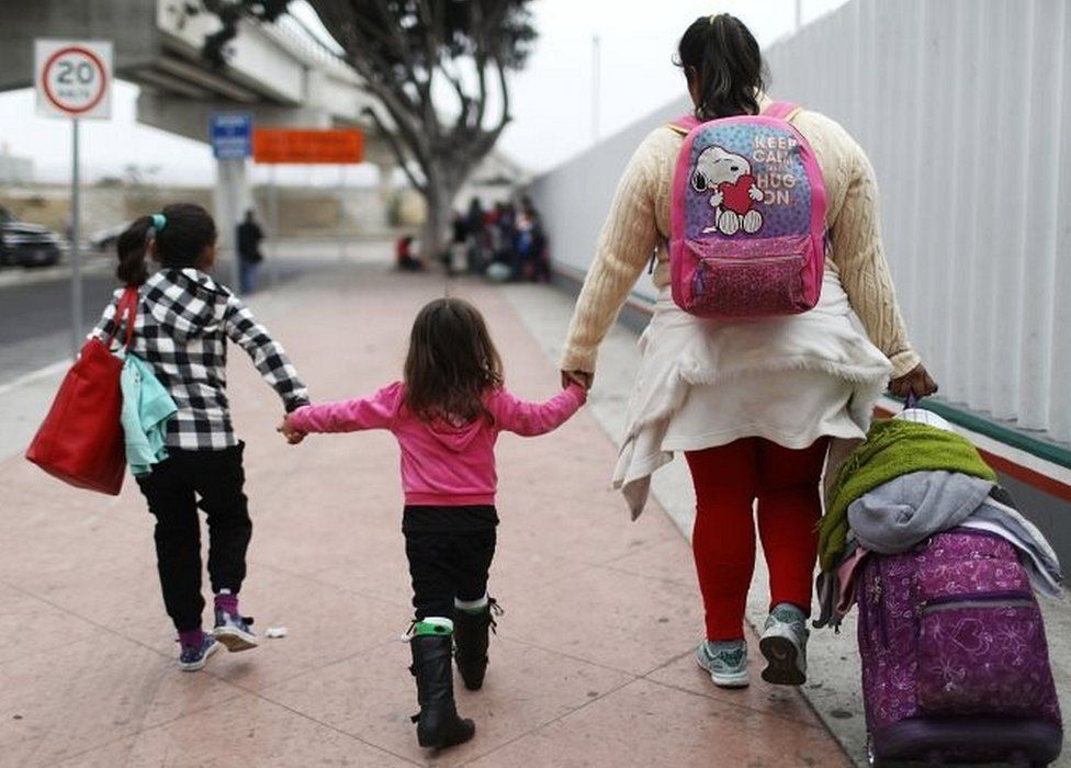 A migrant mother in Tijuana, Mexico, walks with her two daughters and their belongings on their way to the port of entry to ask for asylum in the US