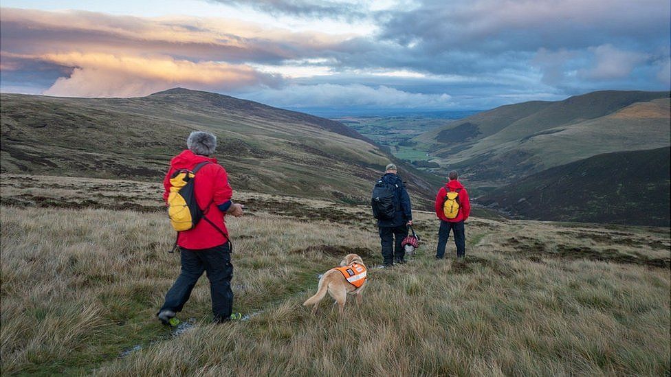 Mountain rescue volunteers escorting man and dog