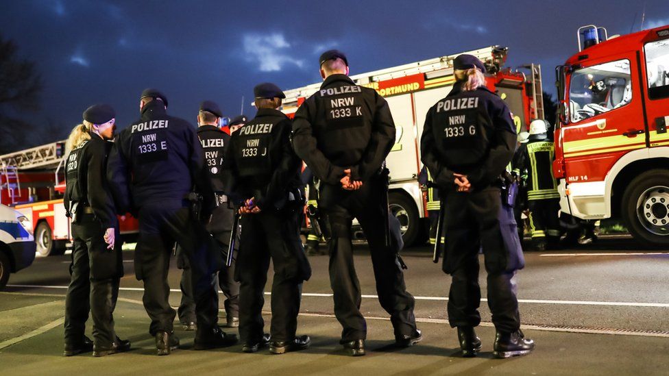 The backs of five police officers, in front of fire engines