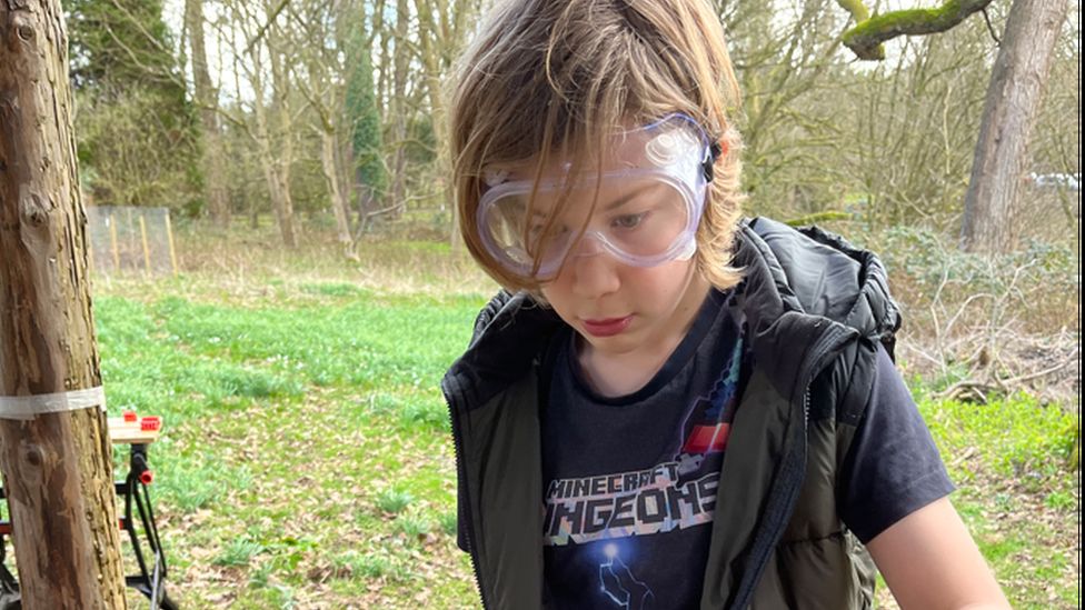 A young boy wearing goggles while doing a science experiment in a wooded area