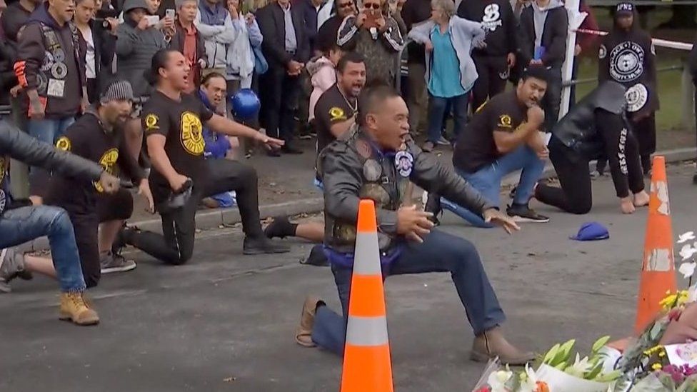 Bikers performing a haka dance next to flowers