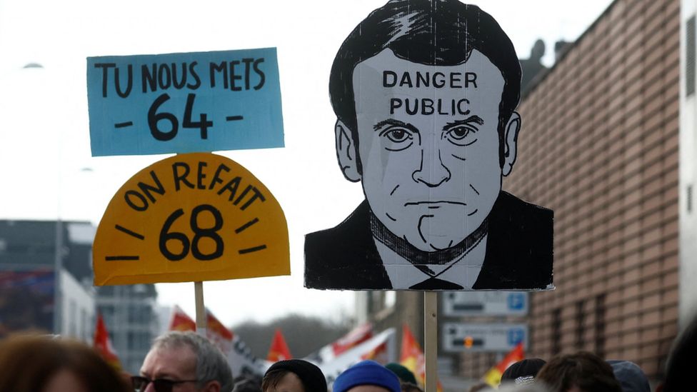 French protesters hold up a sign of Macron reading 'Danger to the public'
