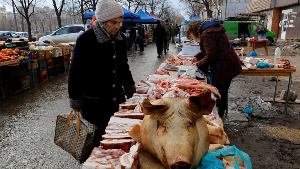 Женщина смотрит на свиное мясо, разложенное на рыночный прилавок в оккупированном Мариуполе