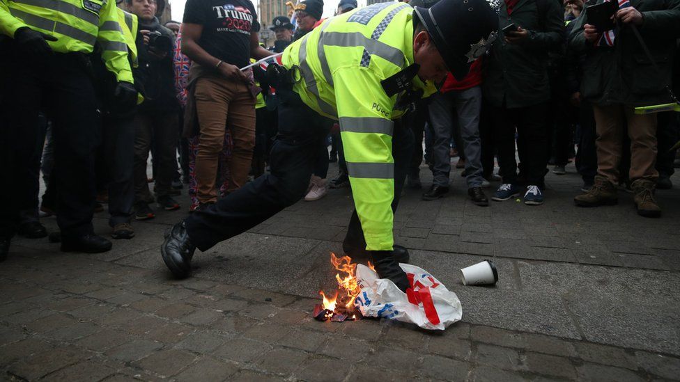 A police officer extinguishes a flag that was set alight by pro-Brexit protestors outside the Houses of Parliament