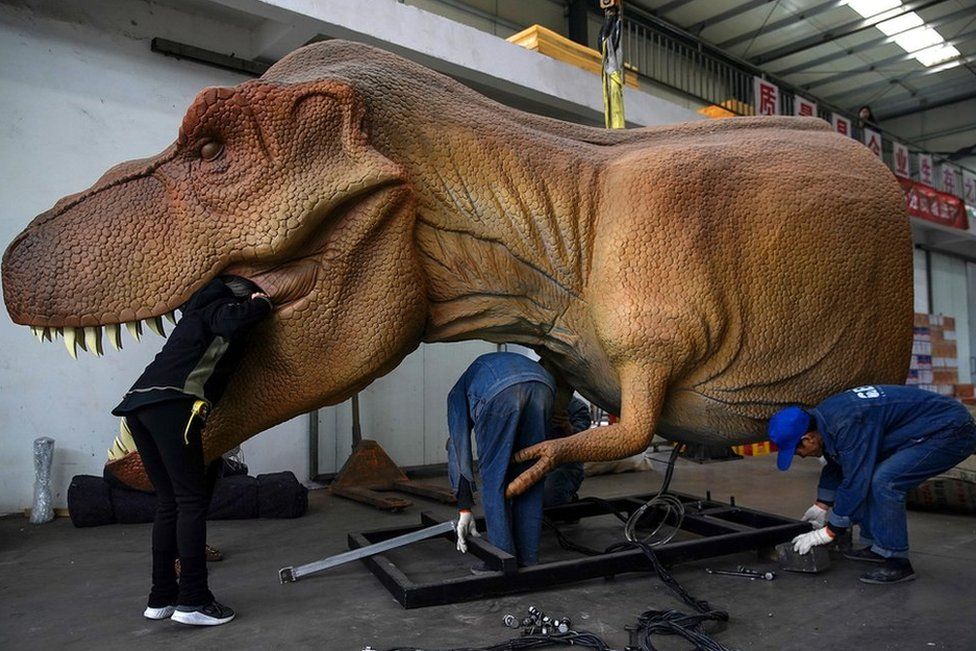 Chinese workers maintaining an animatronic dinosaur at a factory in Sichuan Province, China.