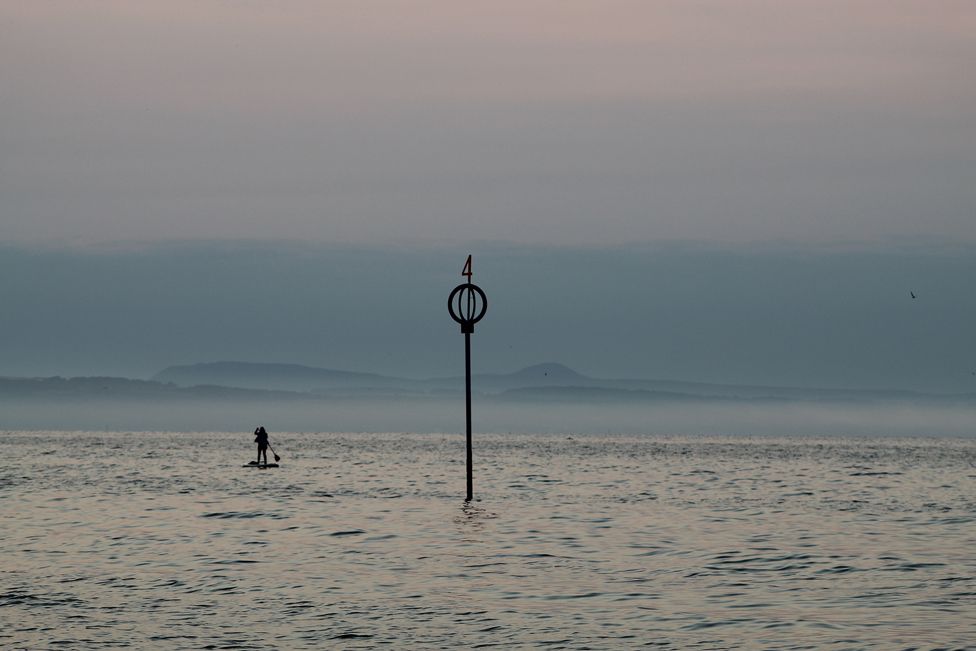 В конце дня - гребец в море, рядом с торчащей из воды металлической конструкцией