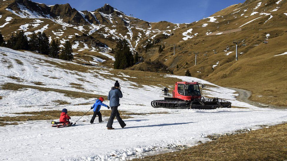 A woman and her child walk next to a snow grooming machine in a snowless landscape on January 2, 2017 in the Swiss Alps resort of les Crosets