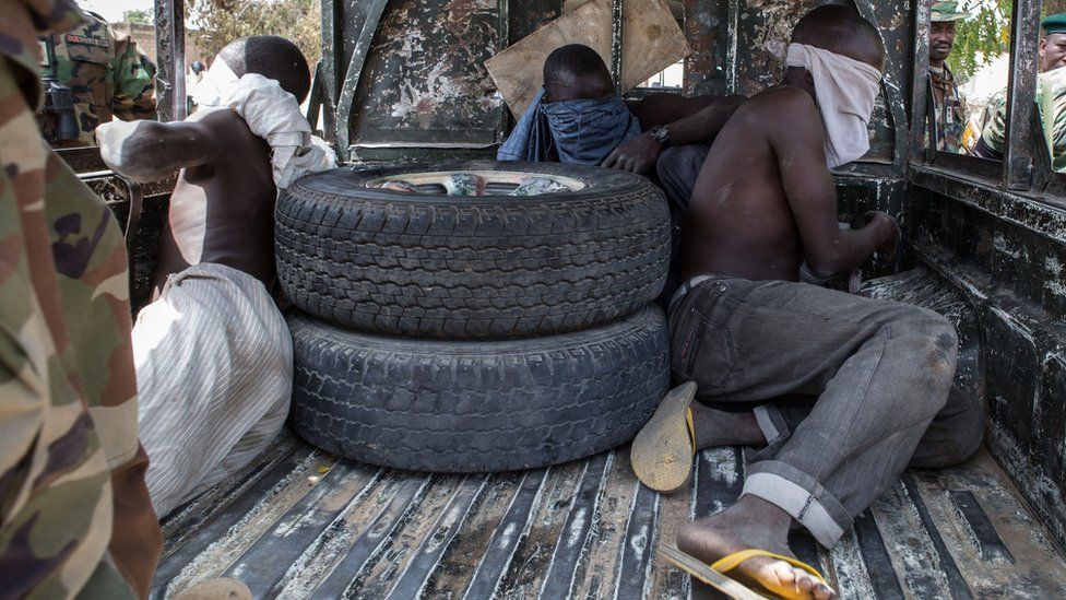 Three young men, who were discovered while entering Bama town, sit blindfolded in the back of a pick-up truck before being taken for interrogation by the Nigerian army on March 25, 2015.